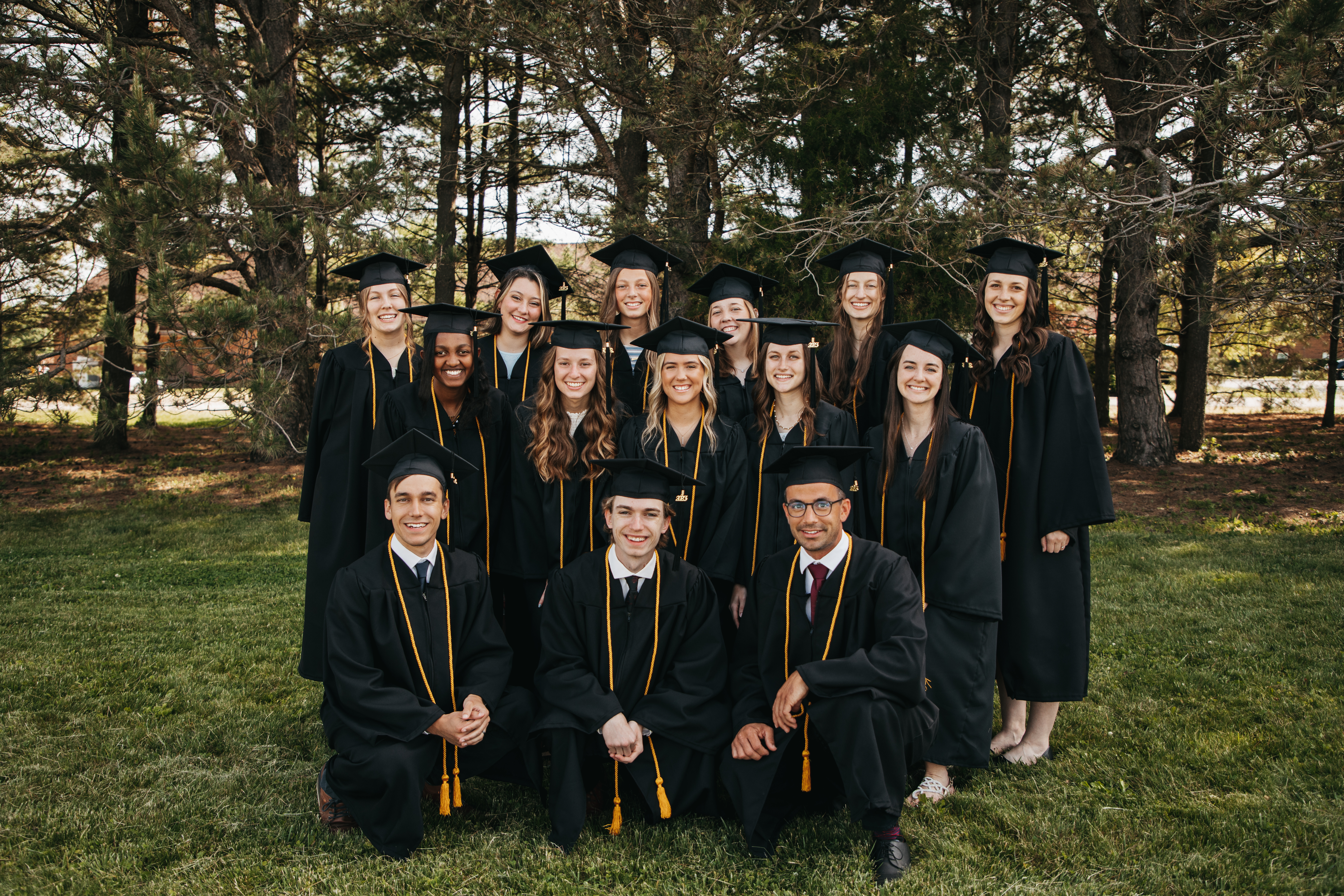 A group of graduates pose with their caps and gowns and yellow cords