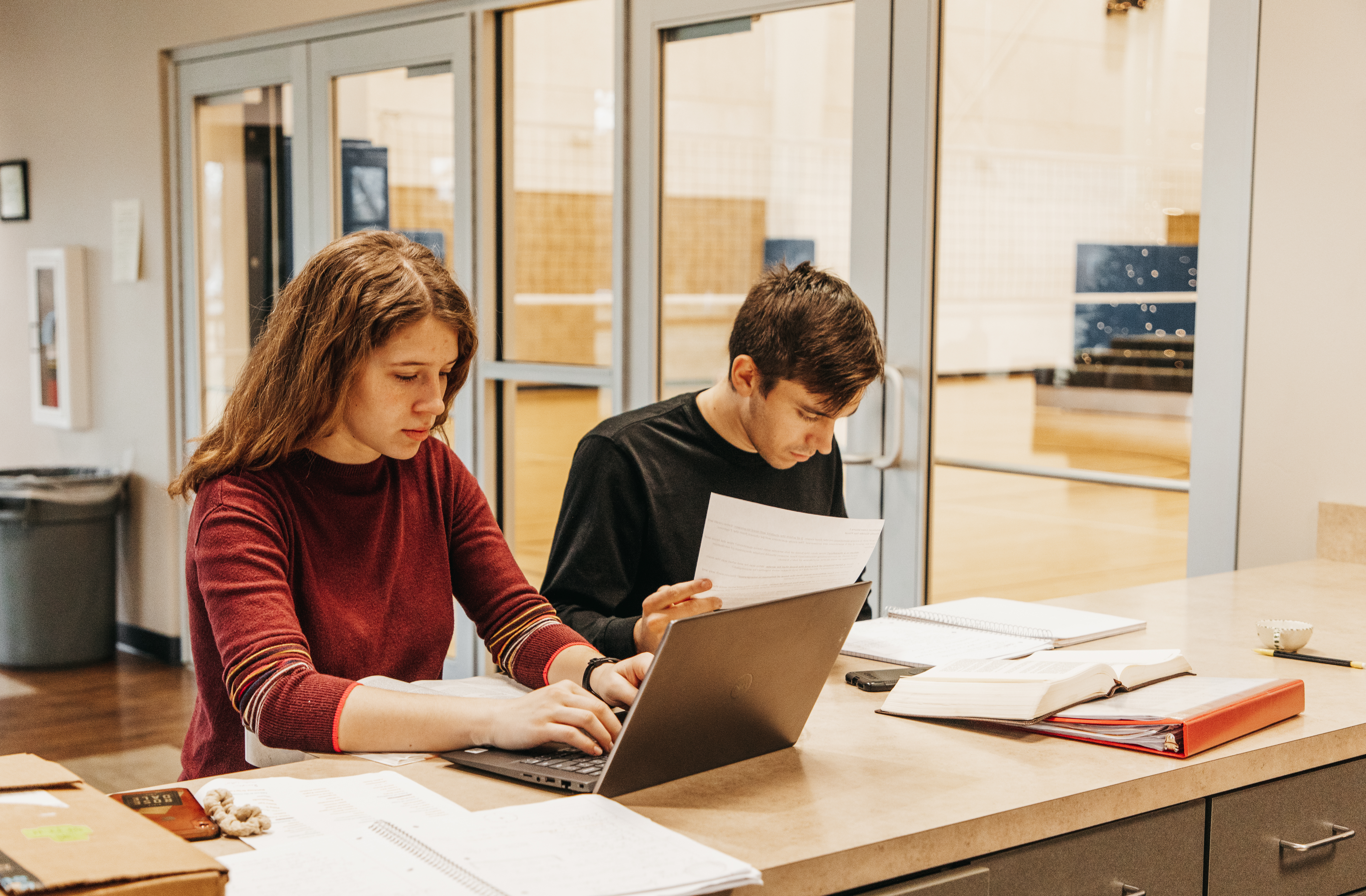 Two students studying with a laptop and books while sitting at a counter.