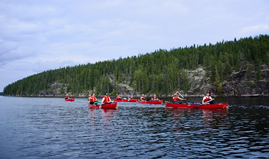 Red canoes on a lake with rocks and pine trees in the background.