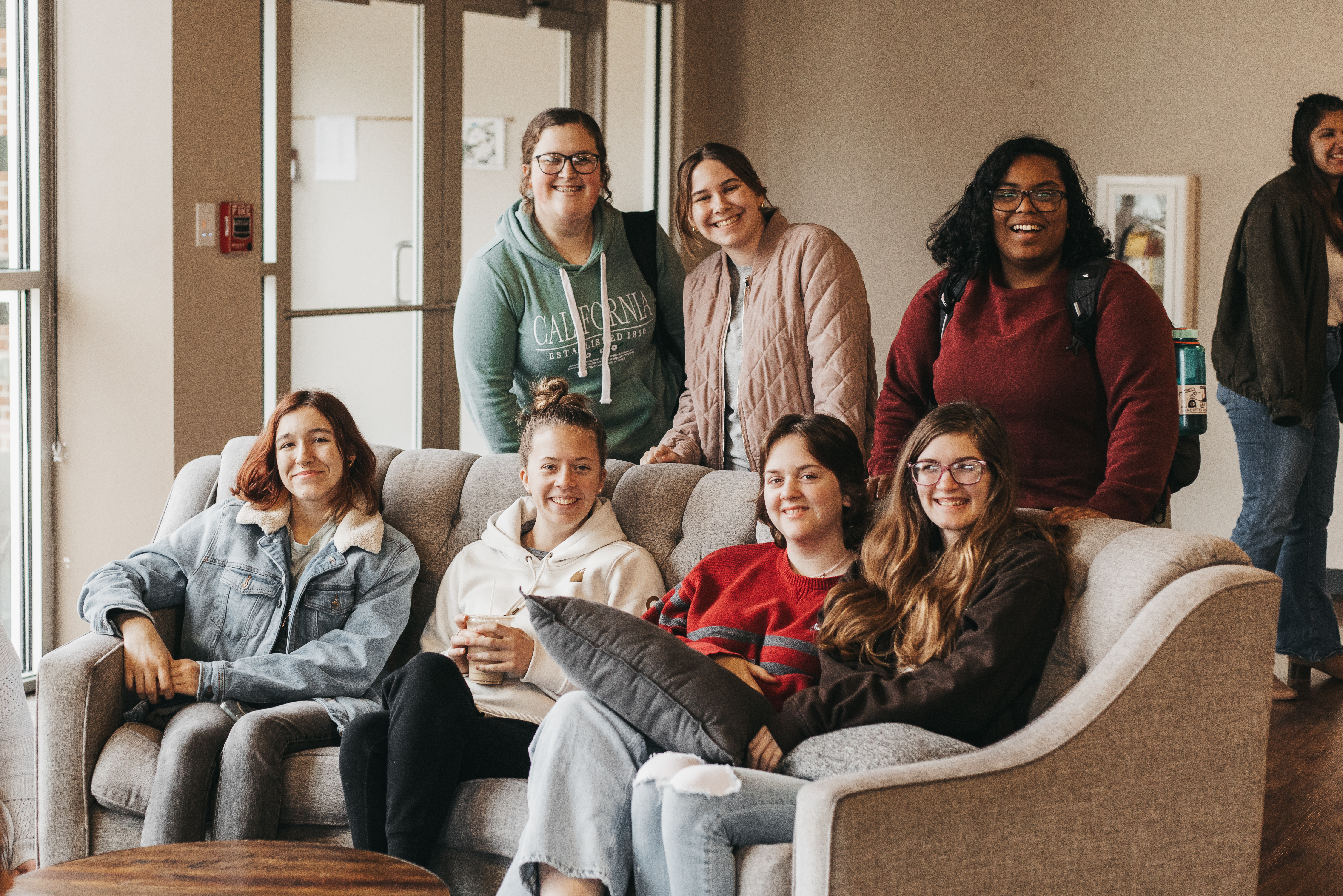 A group of girls smiling while sitting on a couch and standing behind a couch