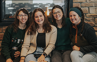 Four RBC students smile while sitting in front of the fireplace in the Student Center