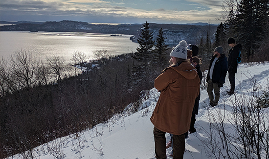 RBC students look out over the snowy top of a mountain to a lake with mountains in the background