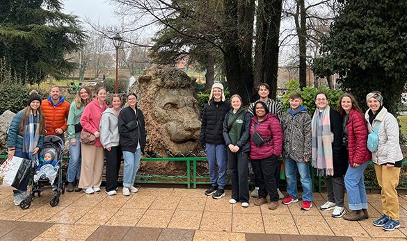 RBC students pose on either side of a lion statue in a park on a cross-cultural trip