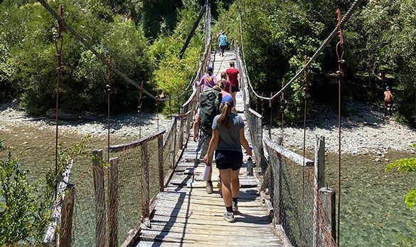 A group of people walking across a suspension bridge above a river.